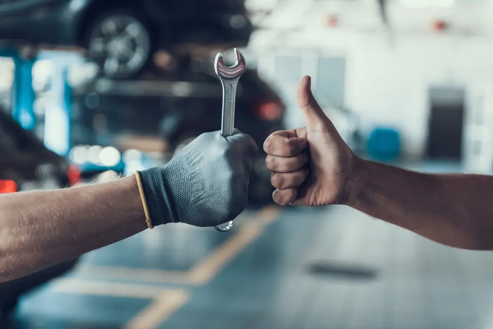 Mechanic holding a wrench and giving a thumbs up in an auto shop, symbolizing quality auto repair services and customer satisfaction at Deutmeyer Auto Advantage.