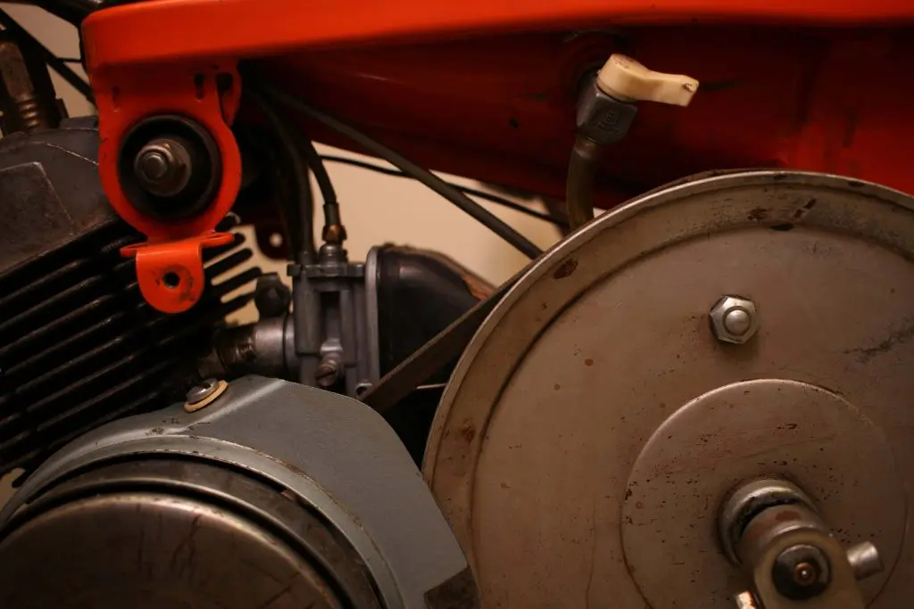 Close-up of a motorcycle engine showing the carburetor, pulleys, and components, emphasizing mechanical details relevant to brake maintenance discussions.