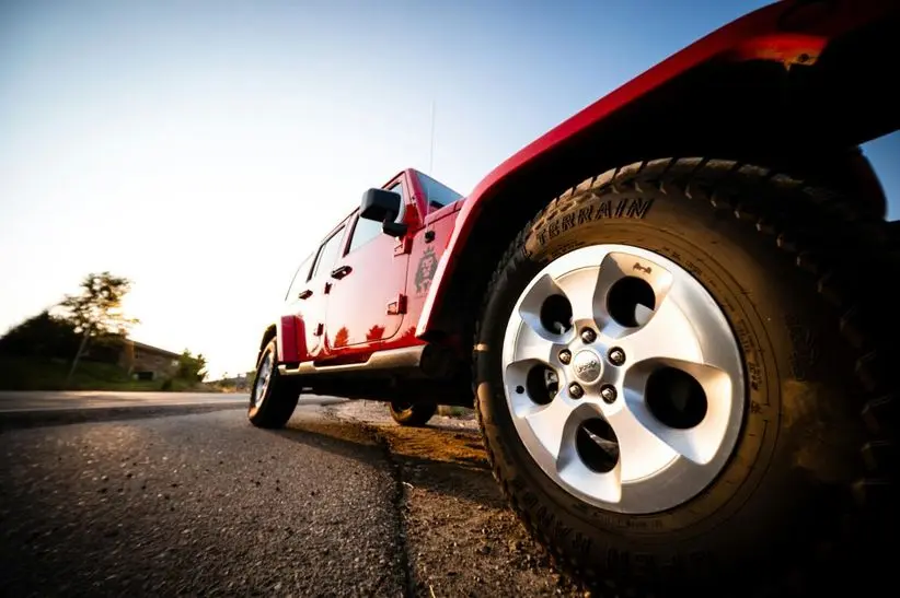 Red all-wheel drive Jeep parked on a road, showcasing its alloy wheels and rugged tires, emphasizing off-road capabilities and vehicle maintenance importance.