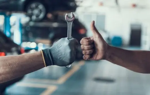 Hands exchanging a wrench and giving a thumbs up in an auto repair shop, symbolizing expert vehicle maintenance and customer satisfaction at Deutmeyer Auto Advantage.