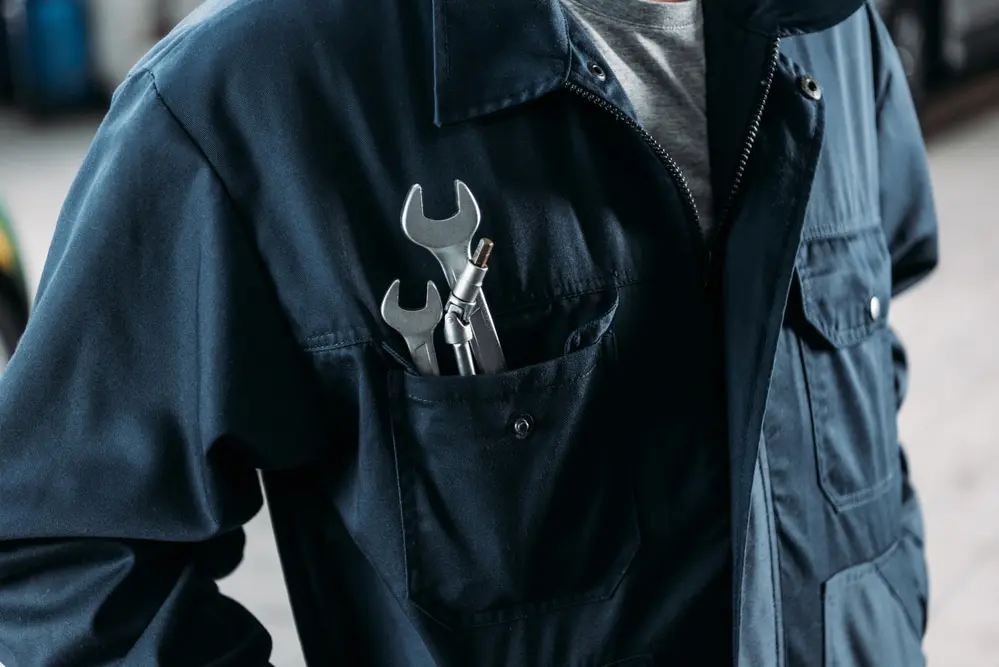 Mechanic wearing a dark blue coverall with wrenches in the pocket, symbolizing auto repair services and maintenance expertise.