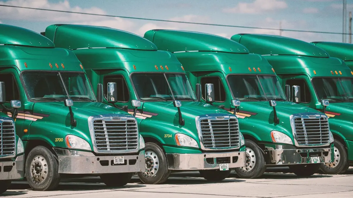 Row of green commercial trucks parked, showcasing their front grills and DOT compliance for safety inspections.
