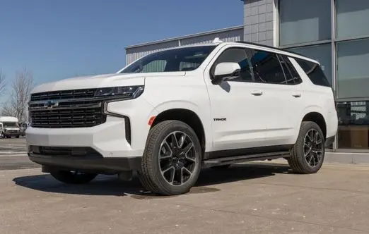 White Chevrolet Tahoe parked outside a modern auto service facility, showcasing its sleek design and readiness for vehicle maintenance.
