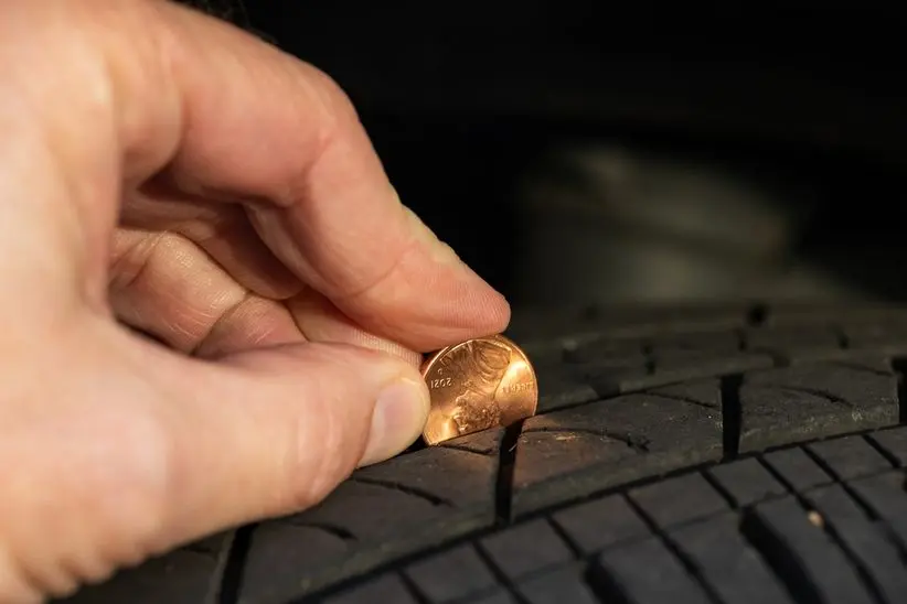 Hand placing a penny into a tire tread, demonstrating a method to check tire depth for winter vehicle maintenance.