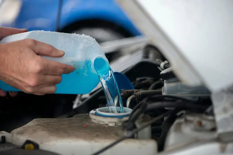 Close up driver pouring blue non freezing windshield glass washer fluid into the tank of the car.