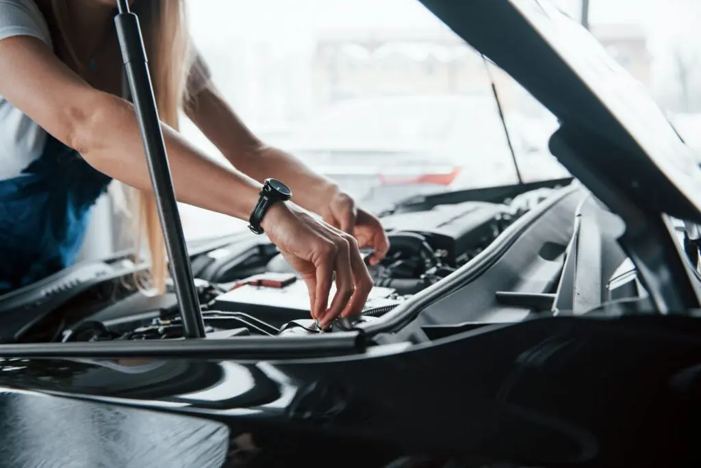 Tuning the details. On the lovely job. Car addicted woman repairs black automobile indoors