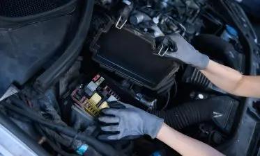 Car repair shop woman checks battery under hood of car Car repair shop woman checks battery under hood of car