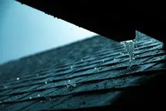Stock photo close-up of rainwater flowing from a gutter on an upper roof elevation and draining onto a lower shingle slope, illustrating roof water movement