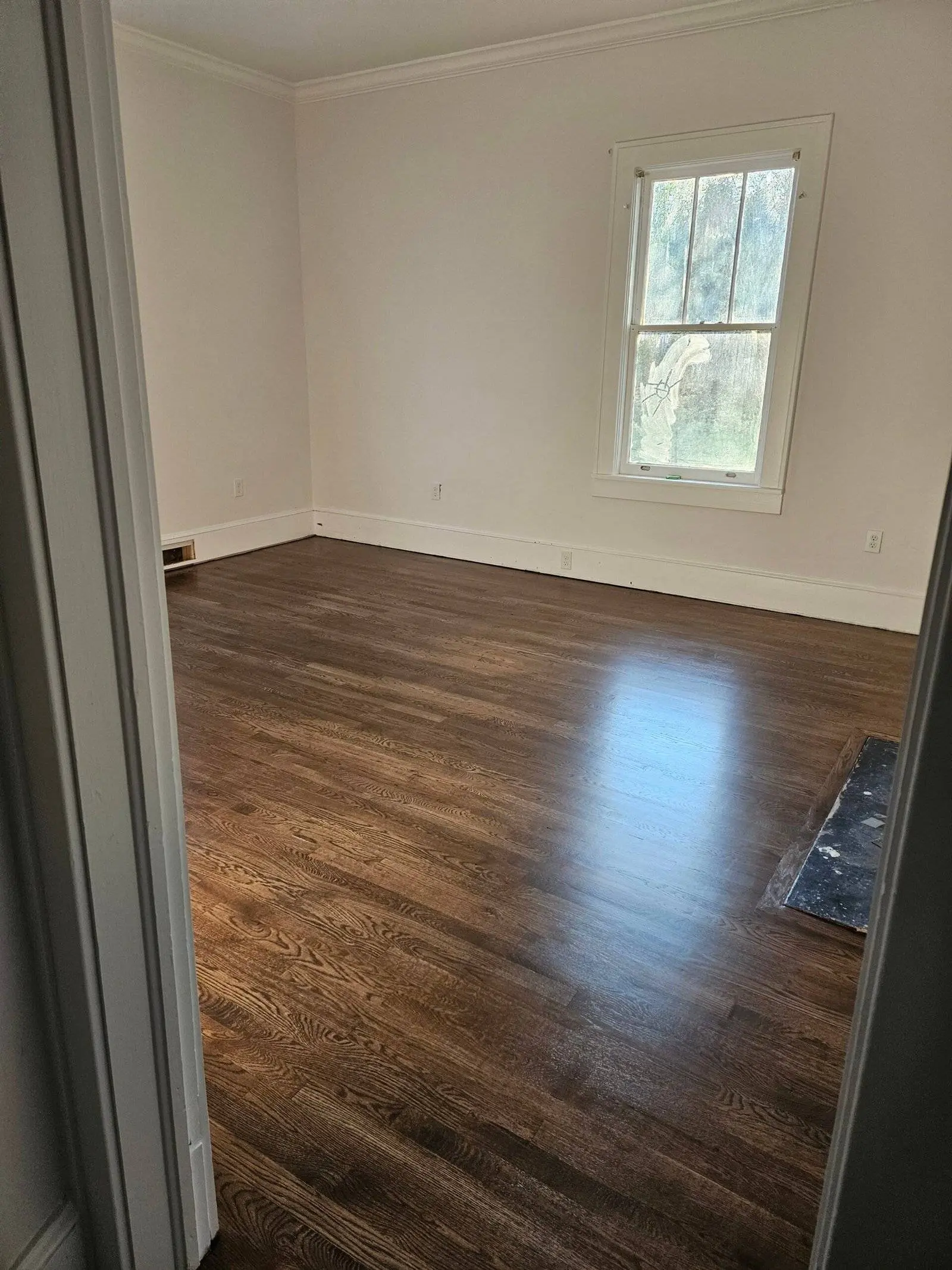 Repaired bedroom with polished hardwood floor, natural light from window, showcasing restoration after water damage from tree impact.