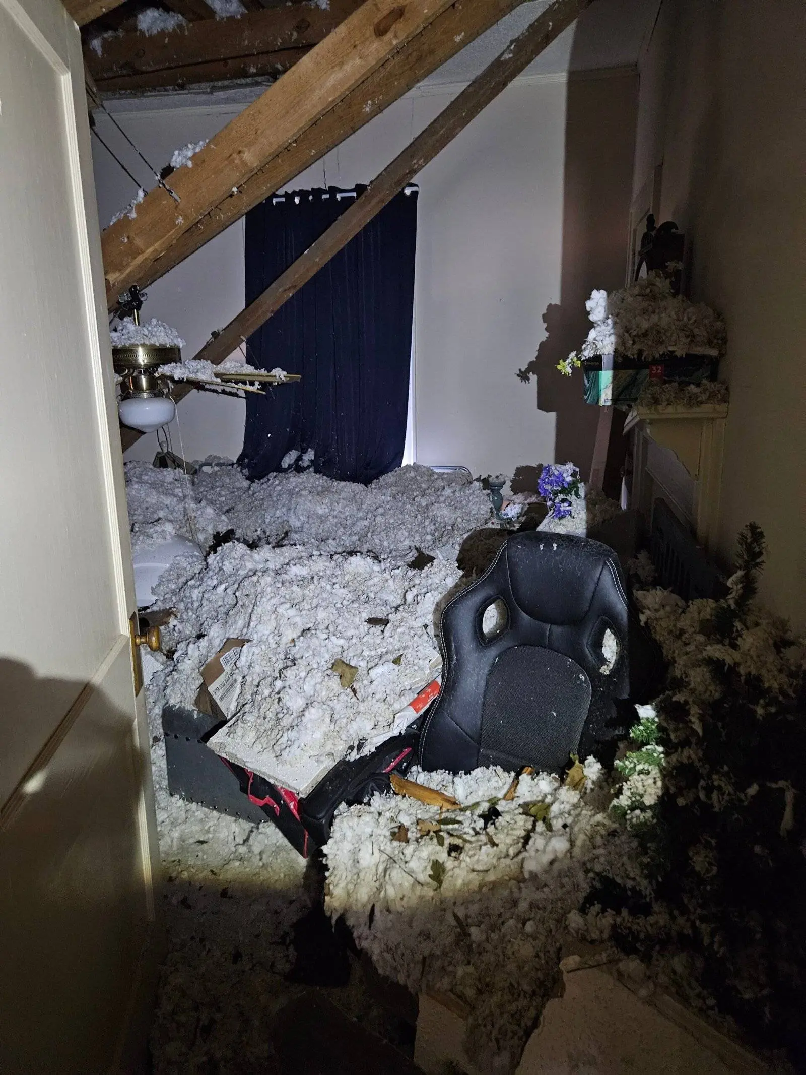 Bedroom interior with collapsed ceiling and debris from water damage, including insulation and fallen materials, following a tree falling on the roof.