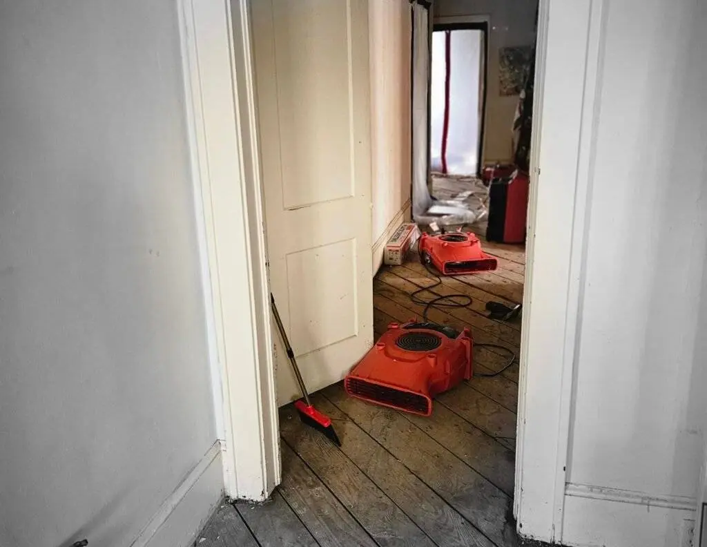 Hallway with industrial-grade dehumidifiers and air movers for water damage restoration, showcasing drying equipment after wet flooring removal.
