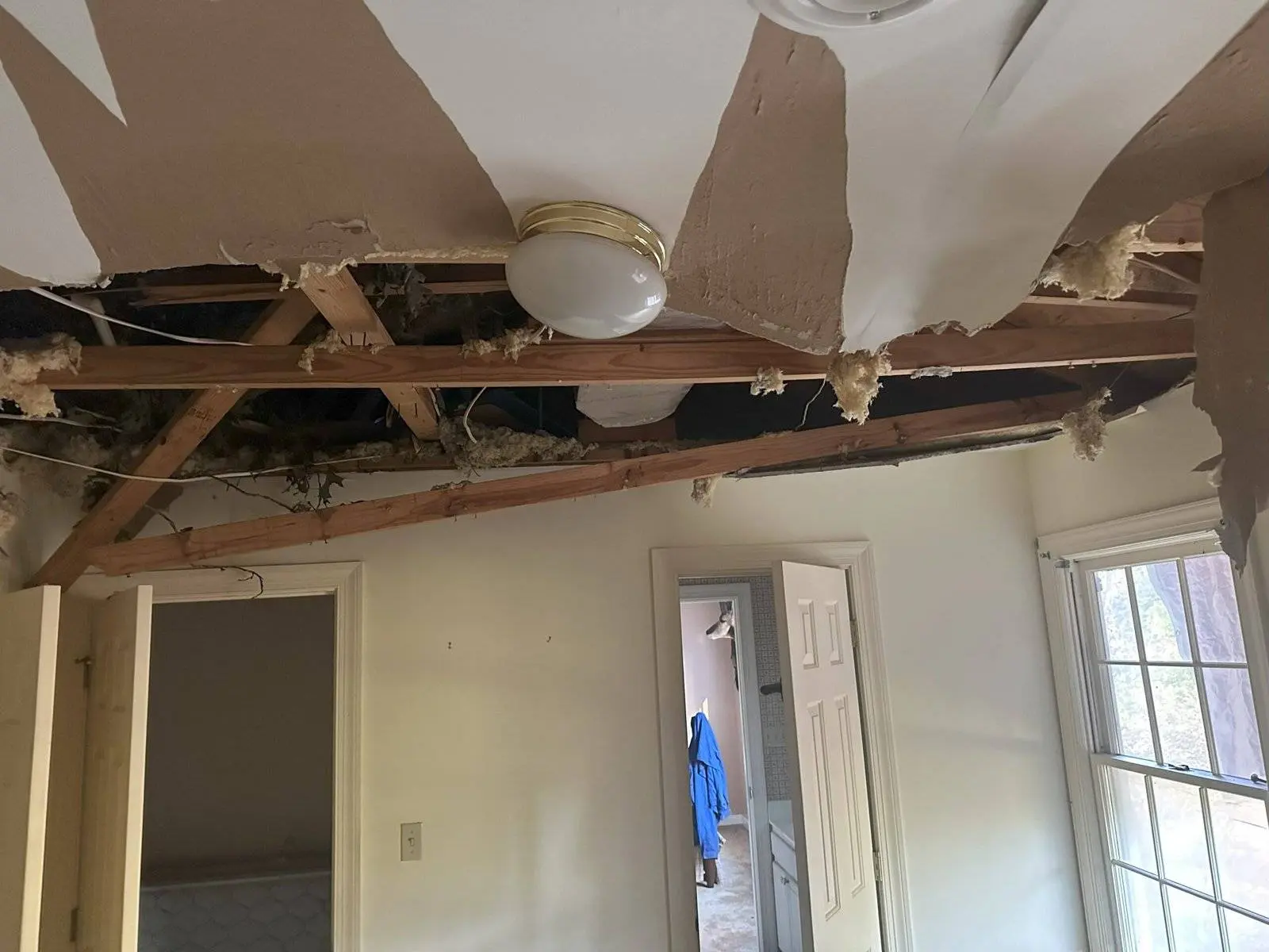 Bedroom ceiling collapsed with exposed wooden beams and insulation due to water damage from a tree, highlighting urgent need for restoration services.