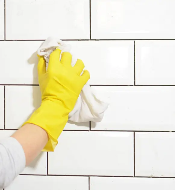 Person wearing rubber glove wiping white wall tile with towel
