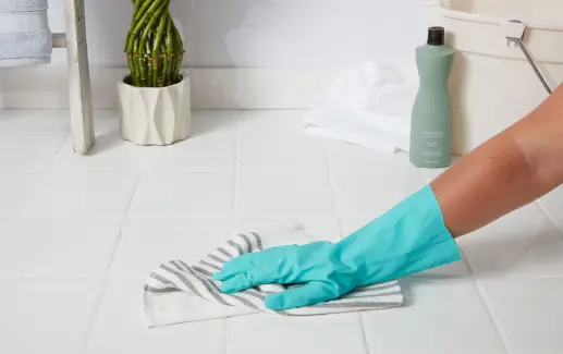 Person wearing rubber glove cleaning white floor tile with striped towel
