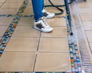 Technician performing professional grout cleaning with extraction equipment