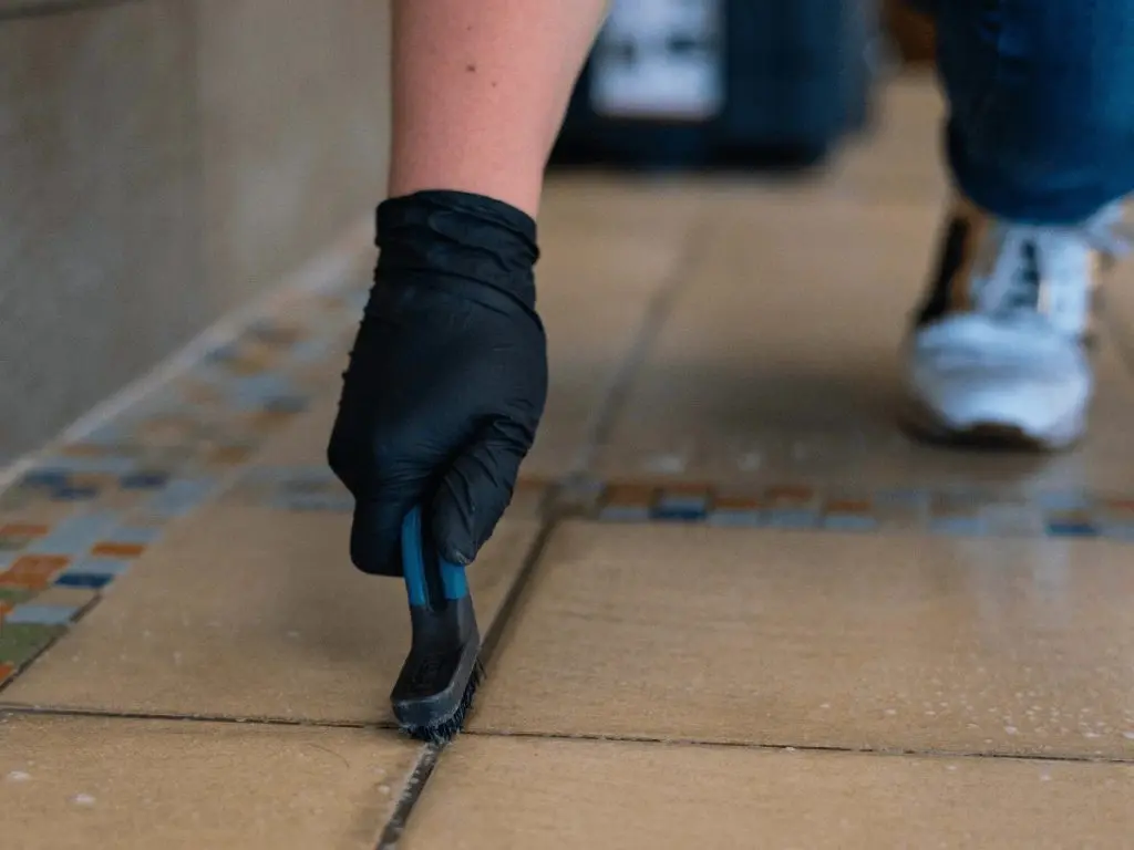 Tucson Tile and Grout worker performing stone tile restoration and grout cleaning on brown floor tiles to make a clean grout