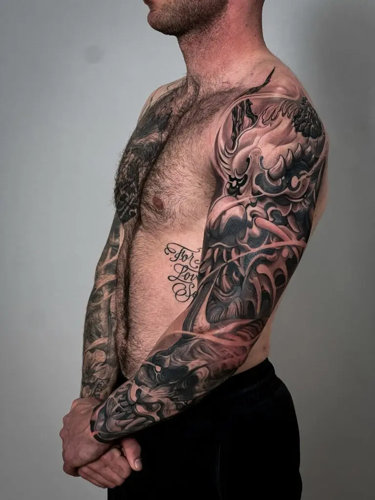 Man displaying full Japanese sleeve and chest piece featuring an oni mask, crashing waves, and rich black shading.