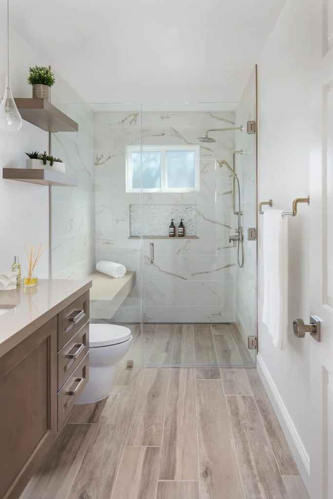 Modern bathroom remodel with a glass-enclosed walk-in shower, marble-look tiles with gold veining, built-in bench, wooden vanity, and recessed niche.