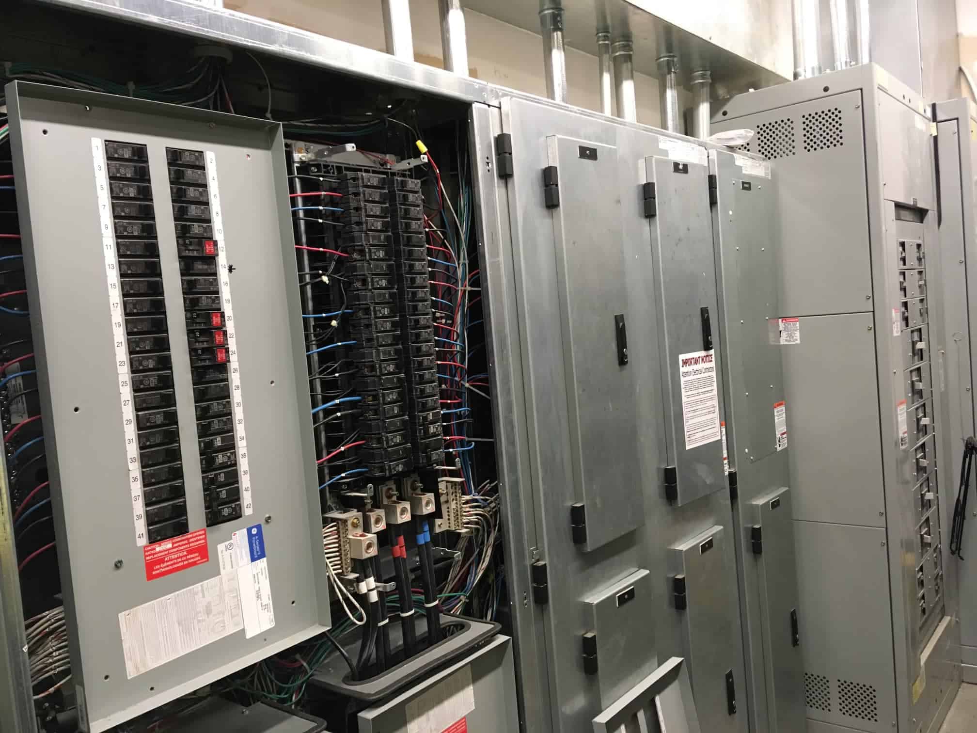 Row of open commercial electrical panels and switchgear in a mechanical room