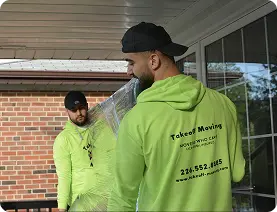 Two movers in bright green shirts carrying a large, wrapped item. Takeoff-Moving Toronto