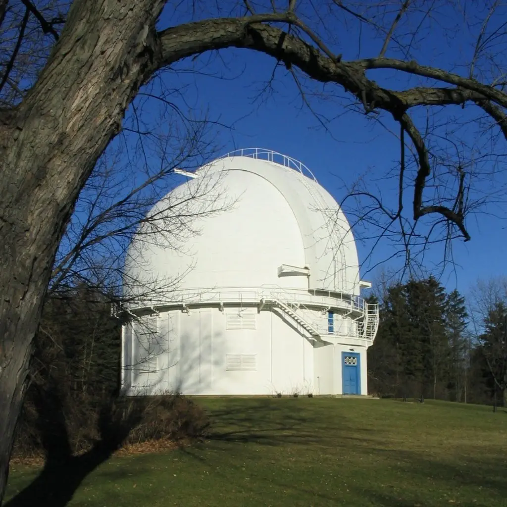 White observatory dome with blue door on a grassy hill under a clear blue sky. Takeoff-Moving Toronto