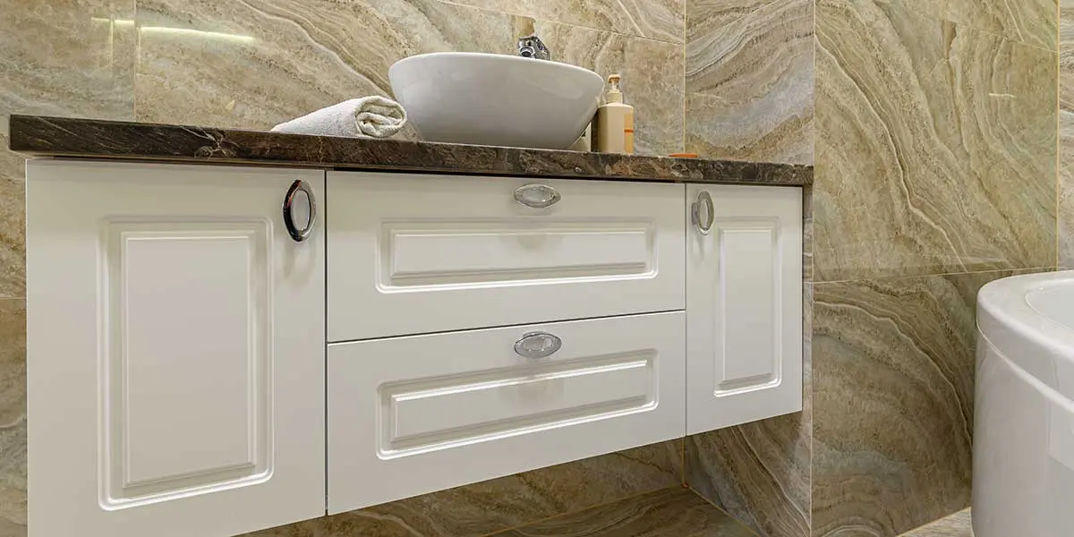 Bathroom Cabinet Hardware Finishes White bathroom vanity with oval silver knobs against marble tiles, showcasing stylish cabinet hardware finishes for modern home design.