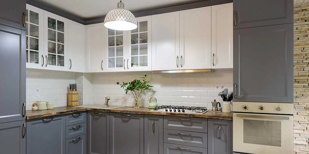 Two-Tone Kitchen Cabinet Guide Modern kitchen featuring white upper cabinets and dark grey lower cabinets, paired with a white tile backsplash and wooden countertops.