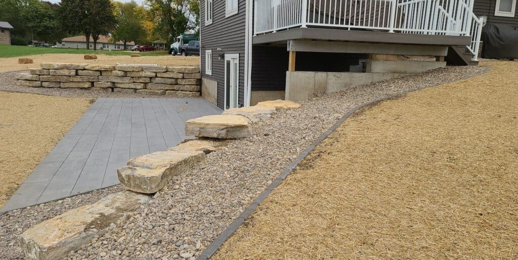 A completed landscaping project featuring a gravel path lined with large decorative stone slabs leading to a stone retaining wall.