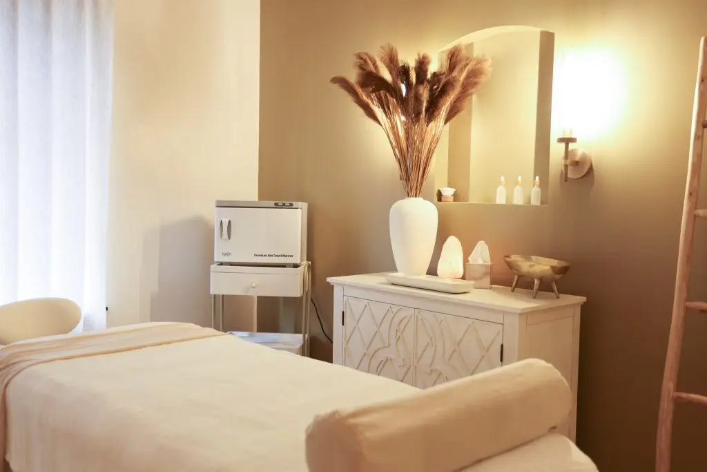 A soothing spa room featuring a massage table, towel warmer, decorative plants, and calming decor, ideal for relaxation and wellness treatments.