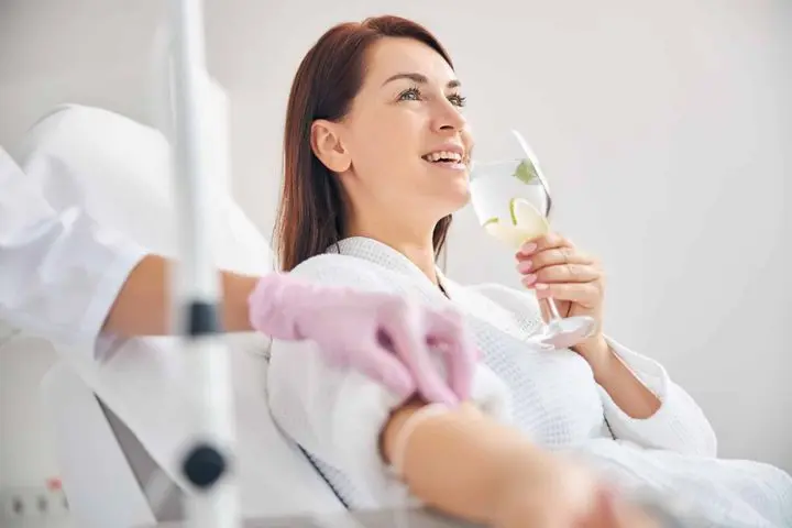 A woman drinking water as she is getting IV hydration Therapy