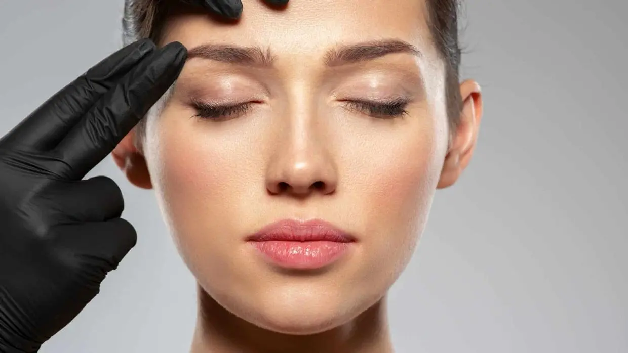 gloved hands looking at a womans eyebrows