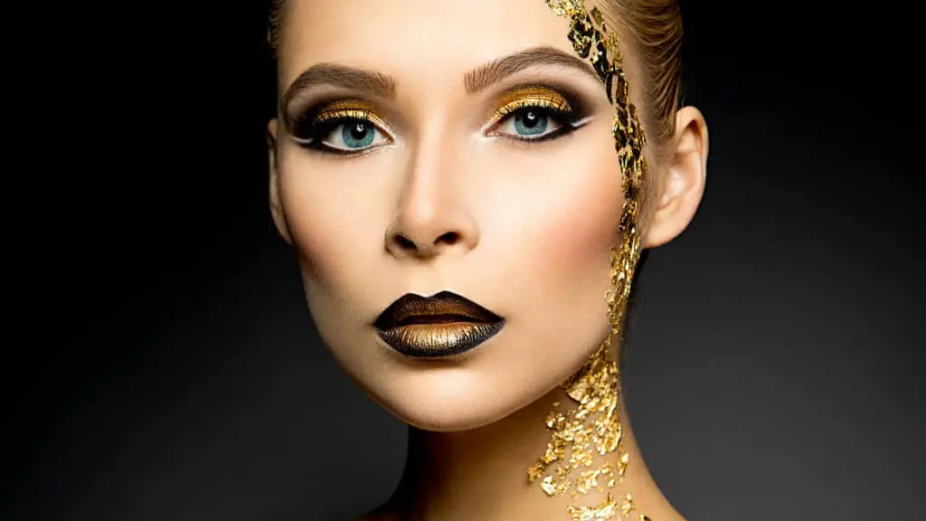A woman with gold makeup and gold leafs down her face and neck