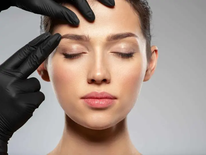 gloved hands looking at a womans eyebrows