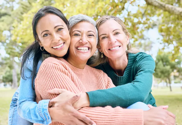 three women smiling and embracing outdoors in park 2026 09 24 14 54 46 utc