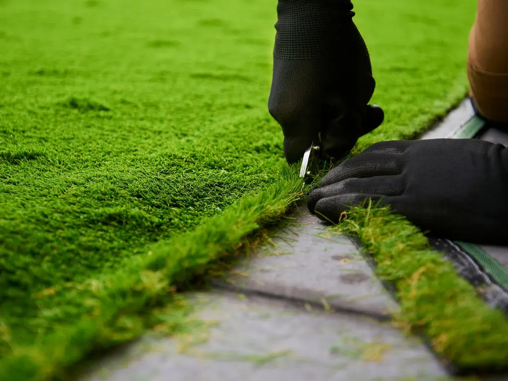professional artificial turf installation with gloved hands trimming synthetic grass edges for a clean finish