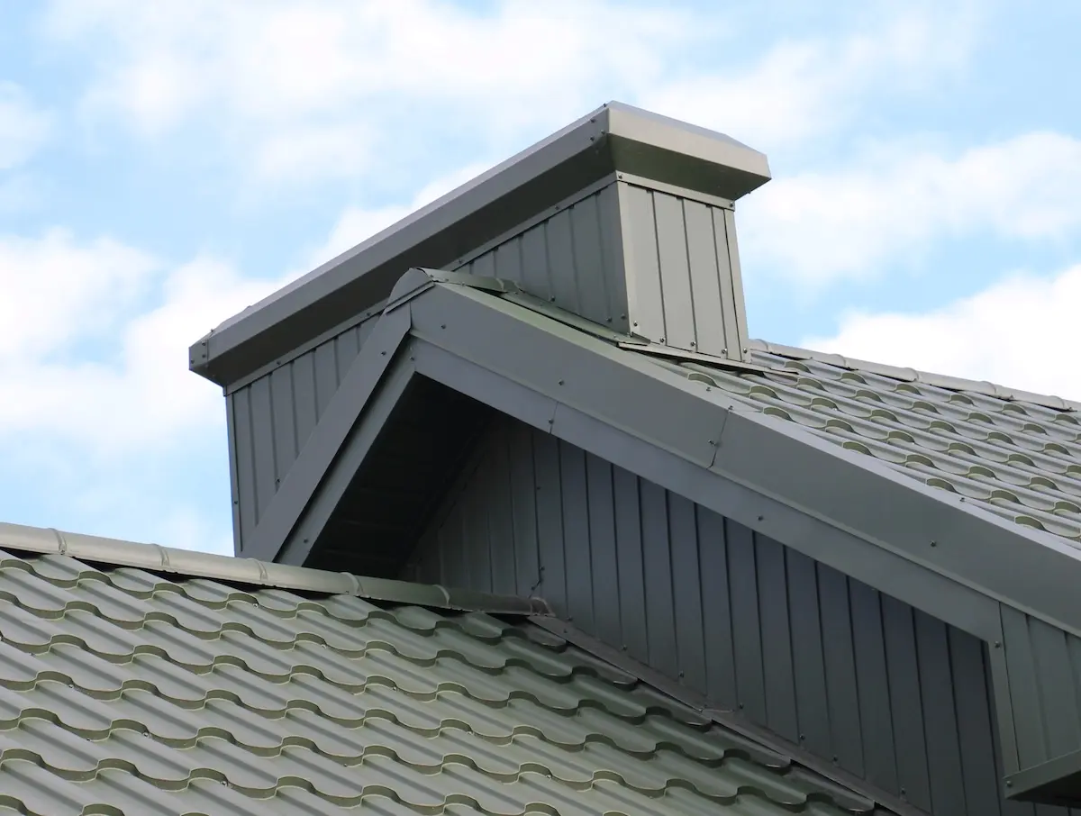 A chimney on the roof of a house covered with metal tiles