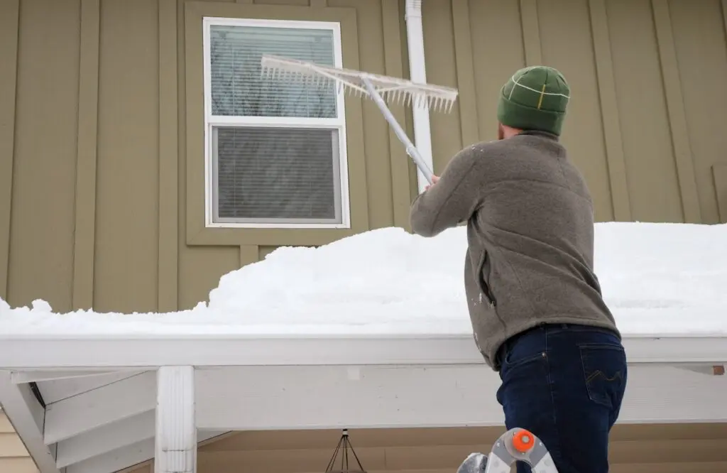 Caucasian man using rake to shovel heavy snow off roof