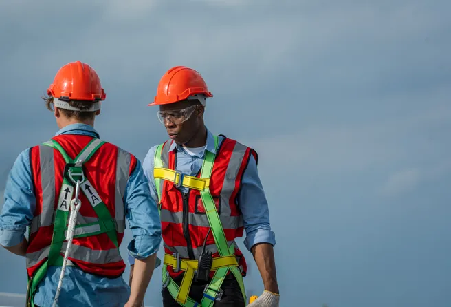 two construction workers wearing safety harnesses and hardhats on top of a roof