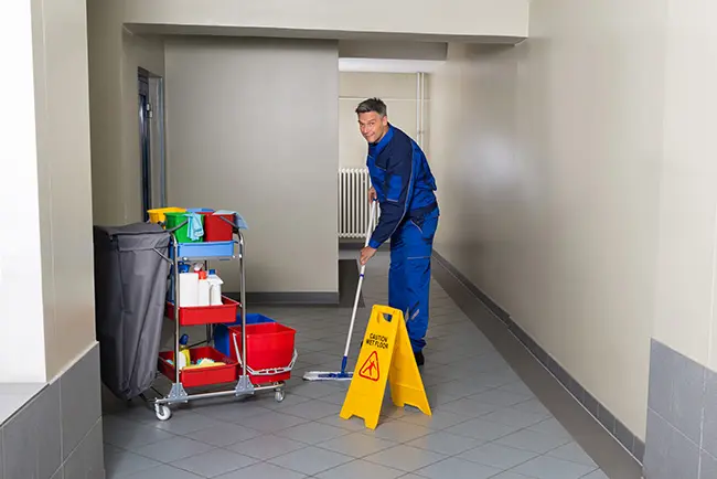 Full length of mature male worker with broom cleaning corridor