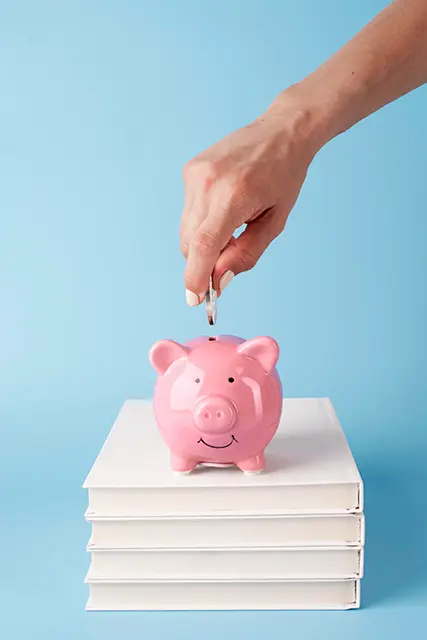 Hand putting more money on a piggy bank