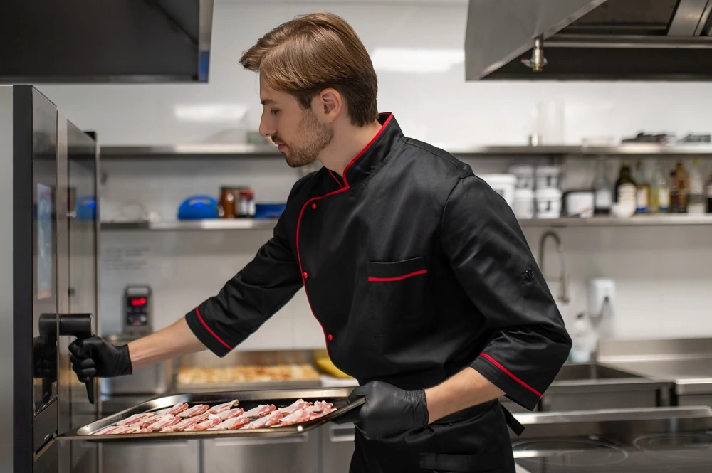Chef placing tray of sliced bacon into commercial oven