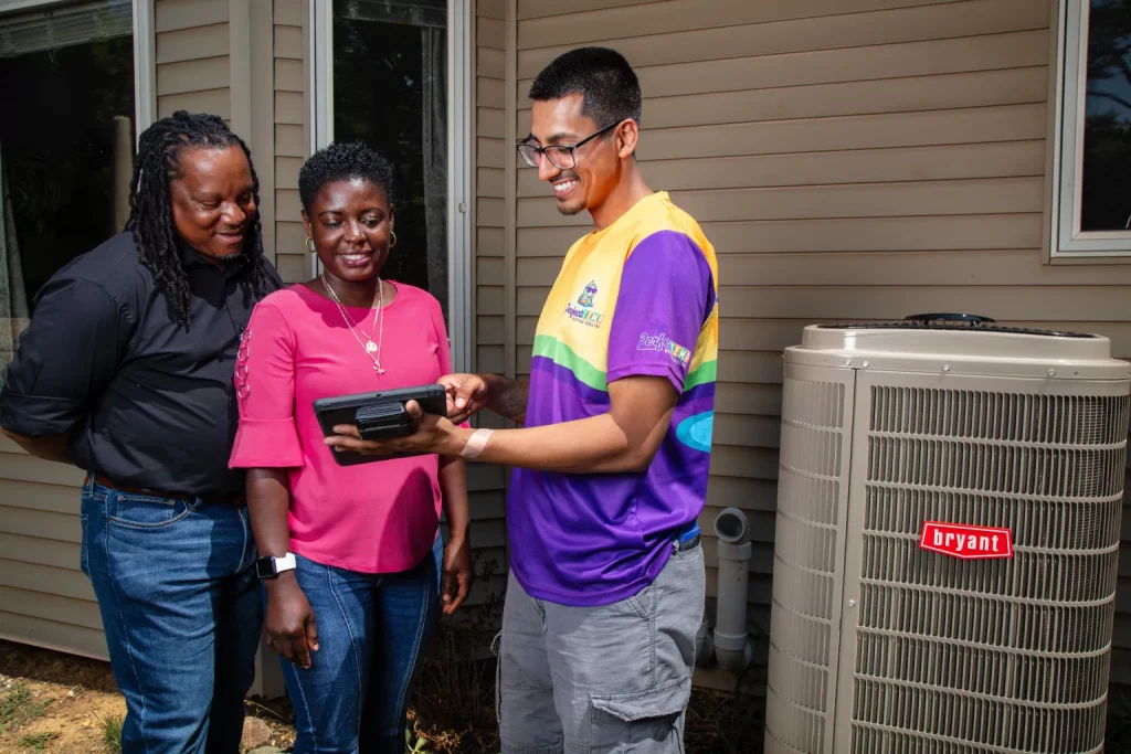 perfect temp technician showing tablet screen to african american couple next to a heat pump