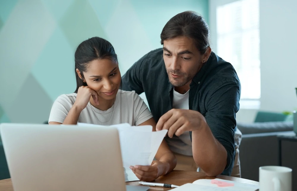 smiling couple looking at paperwork and laptop