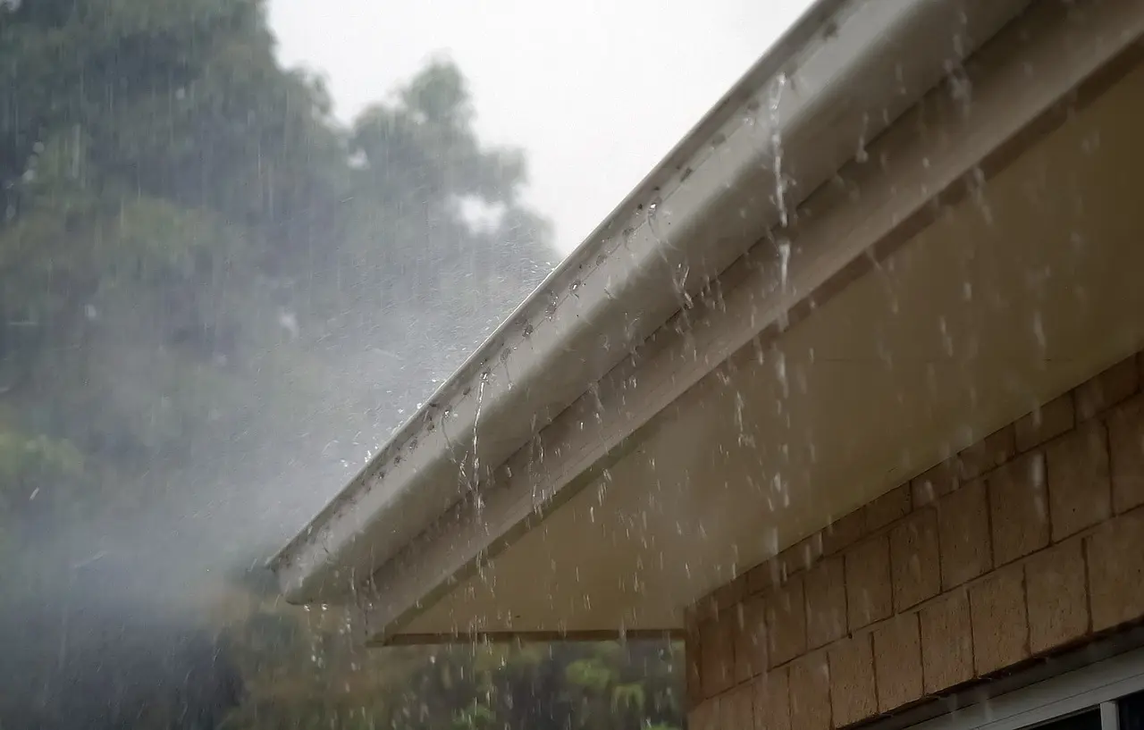 A house with gutters on the side of its roof that is under a downpour.