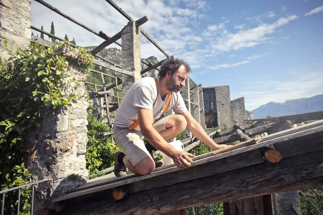 A man in a shirt and shorts repairing his roof.