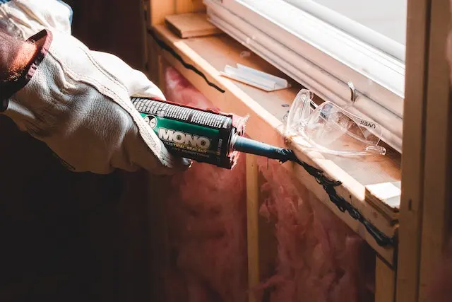 Man applying caulk to window area to prevent damage.