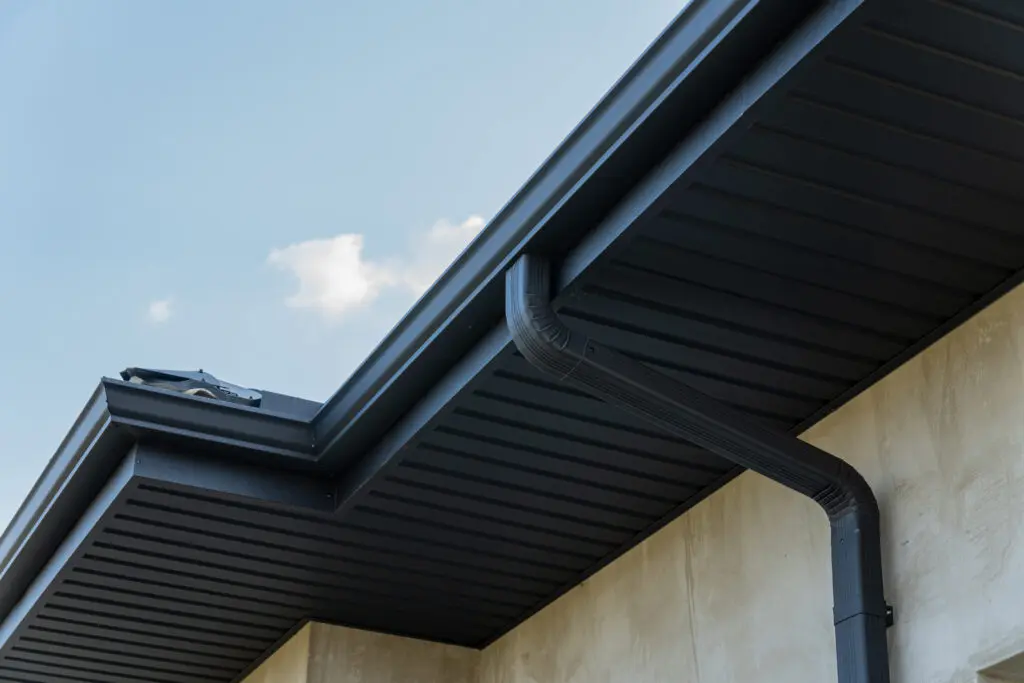 gutter downspouts Close view of a roof edge and downspout against a bright blue sky highlights contemporary construction features and materials.