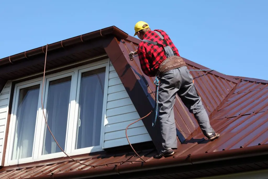 roofer builder worker with pulverizer spraying paint on metal sheet roof