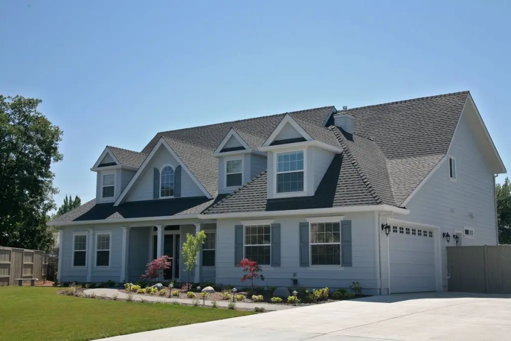 big white house with grey shingles roof under blue sky summer time
