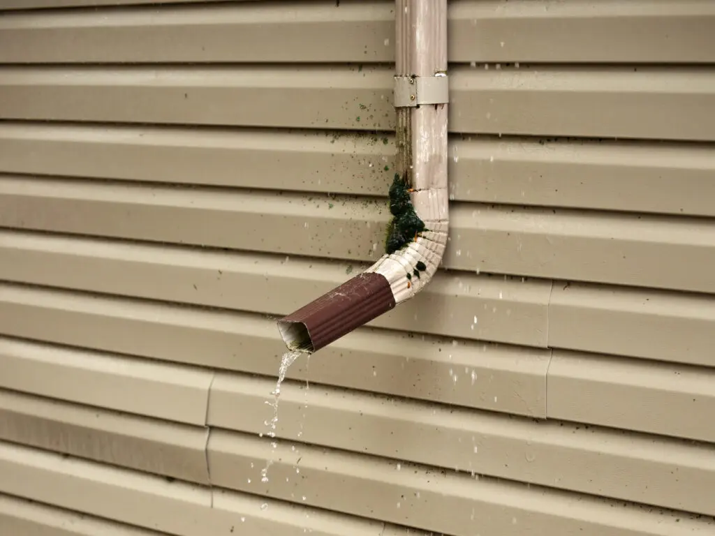 gutter downspouts Rain Water Pours Out of a Short Downspout on side of house pooling by foundation because of improper drainage design and inadequate extension length. Pooled water threatens to flood basement foundation. High quality photo